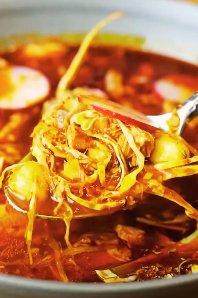 Pozole simmering in a large pot with rich red broth